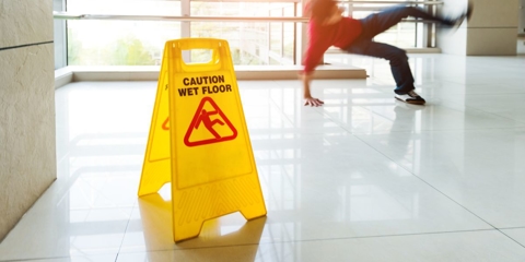 wet floor sign on a tile floor, you can see a person mid-fall in the background