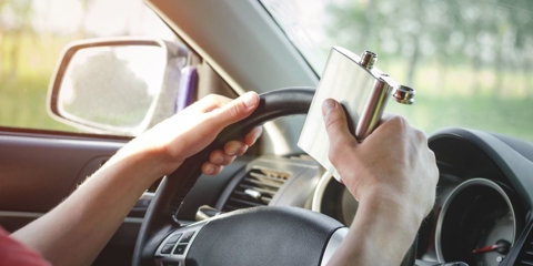 close up of a person holding a flask on their steering wheel